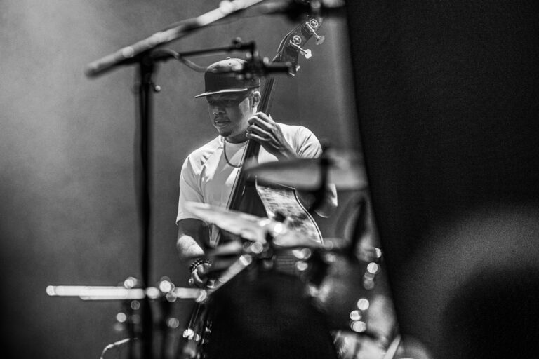 Een muzikant speelt basgitaar op het podium, omgeven door muziekinstrumenten.