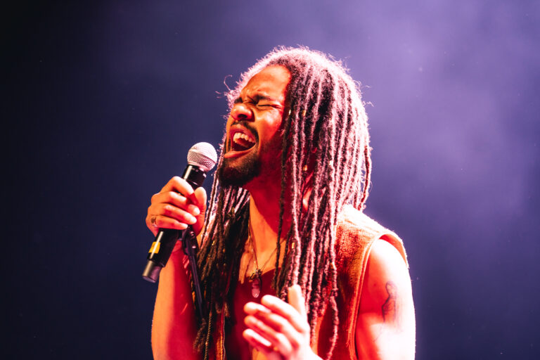 Een man met rastahaar die uit volle borst in een microfoon zingt.