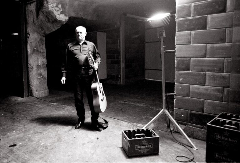 Zwart-wit foto van Lee Clayton met zijn gitaar in één hand.