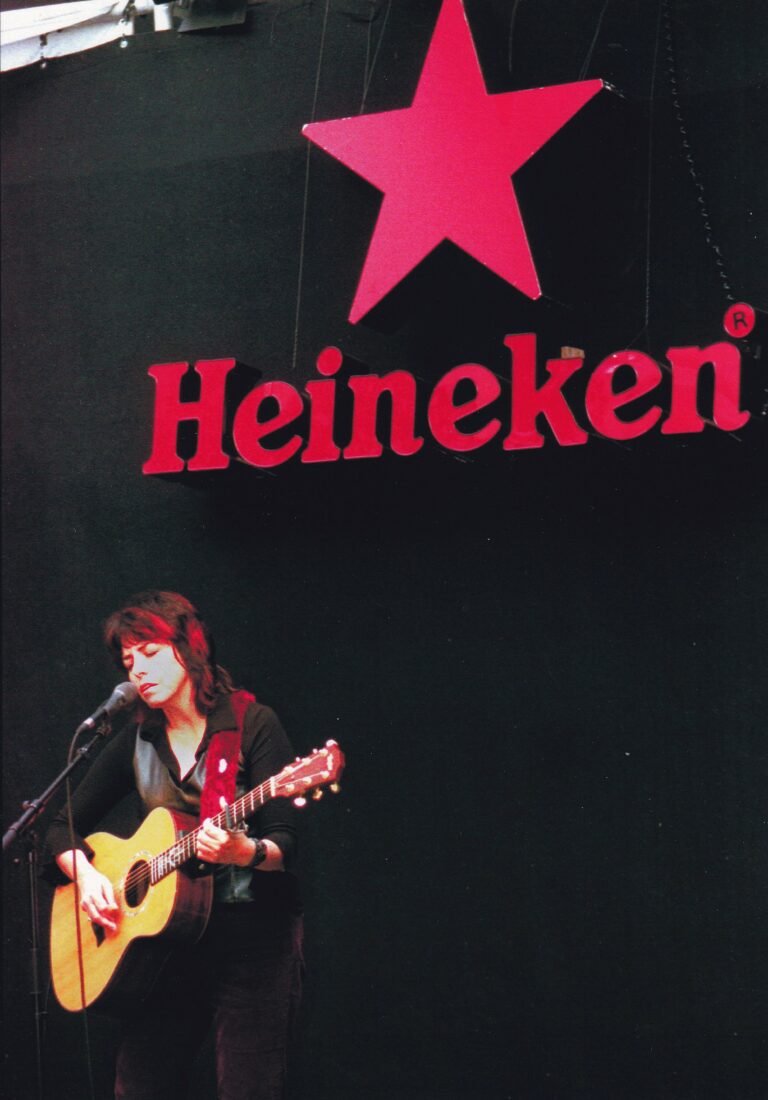 Een muzikant met een gitaar zingt op een podium met een Heineken-logo op de achtergrond.