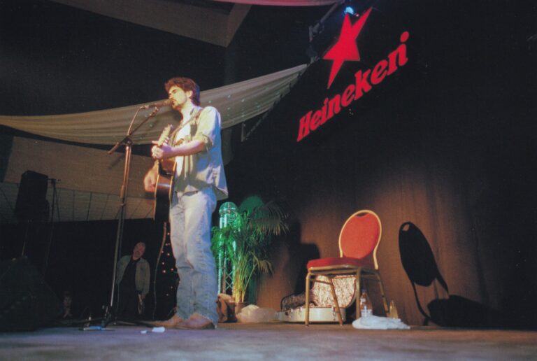 Een muzikant speelt gitaar op een podium, met een grote rode ster en de naam 