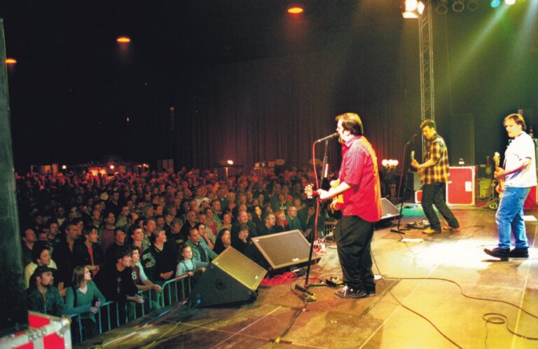 Een muzikant staat op het podium voor een groot publiek tijdens een concert.