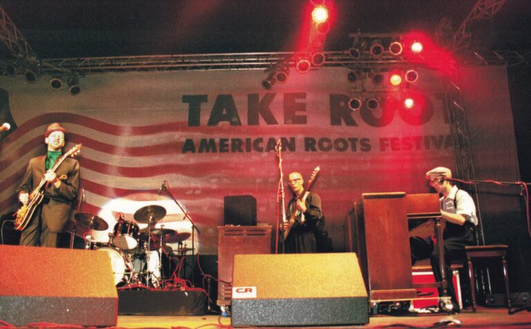 Een liveband speelt op een podium met een groot spandoek dat 