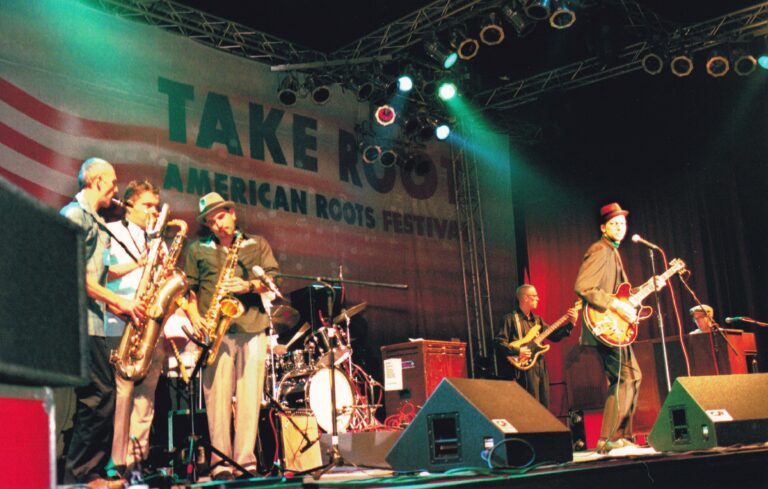 Een band speelt live op een festival met verschillende muzikanten en instrumenten op het podium.