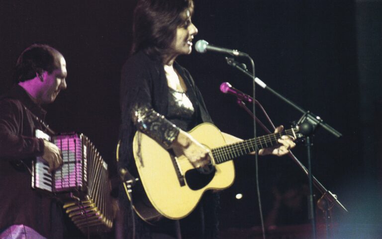 Een muzikant die op een podium een gitaar speelt en zingt.