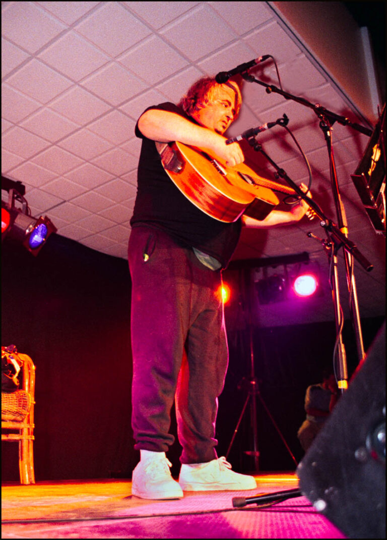man met een gitaar op een podium