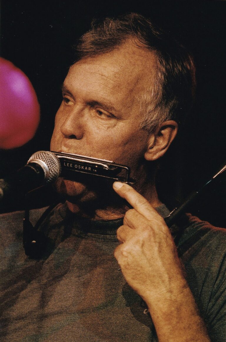 Man met grijs haar die voor een microfoon op een mondharmonica speelt