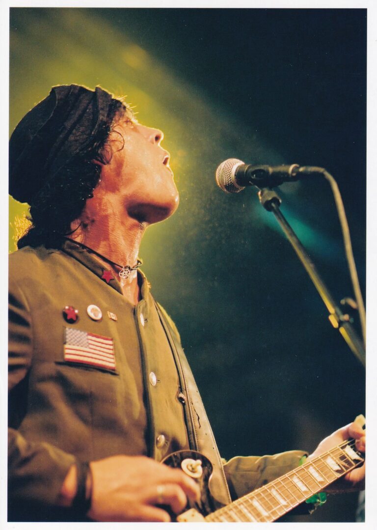 man met een hoedje op die aan het zingen is en wordt begeleidt met een gitaar