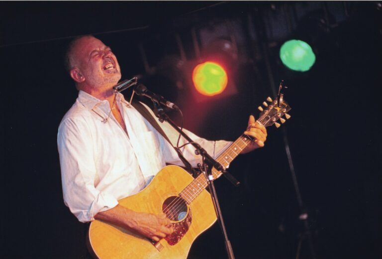 Een man zingt en speelt gitaar op een podium met gekleurde lichten.