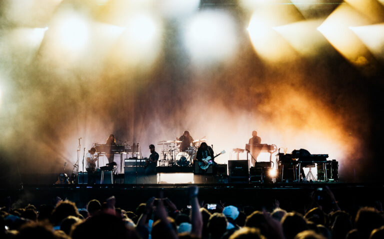 De 7 bandleden van The War On Drugs in actie op een groot podium met veel kleurrijke lampen.