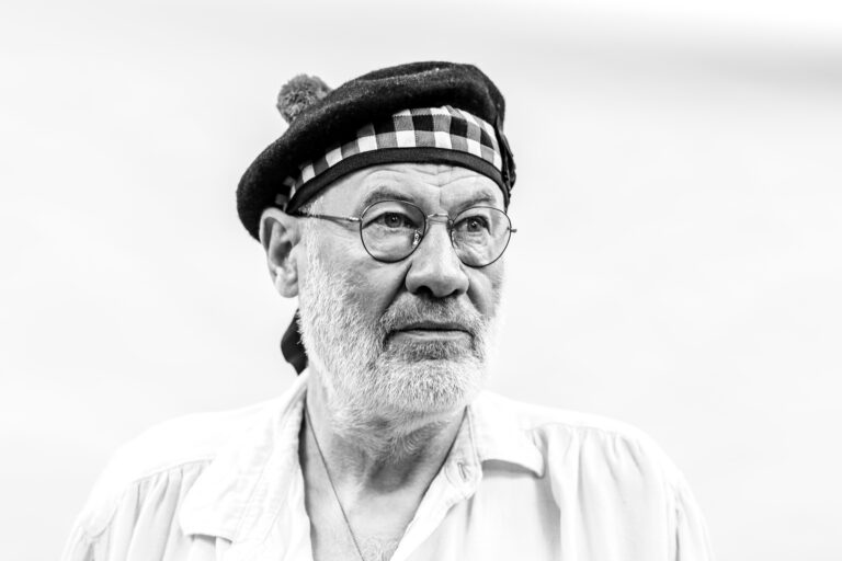 Een zwartwit portretfoto van één man, Fish, die met een baret op zijn hoofd naar de zijkant kijkt.