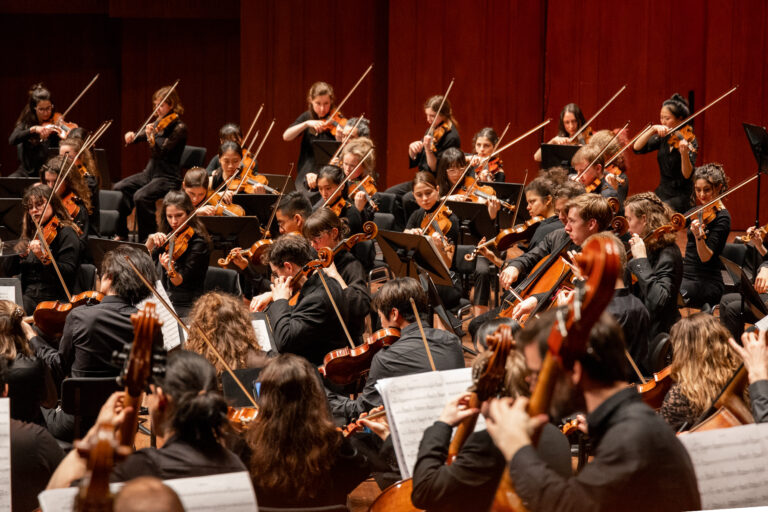 Een groot orkest speelt muziek op een podium, met musici die verschillende instrumenten bespelen.