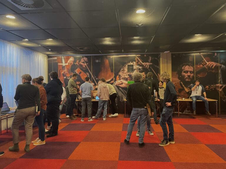 Een drukke lobby van een bioscoop met mensen die staan en praten voor grote muurschilderingen.