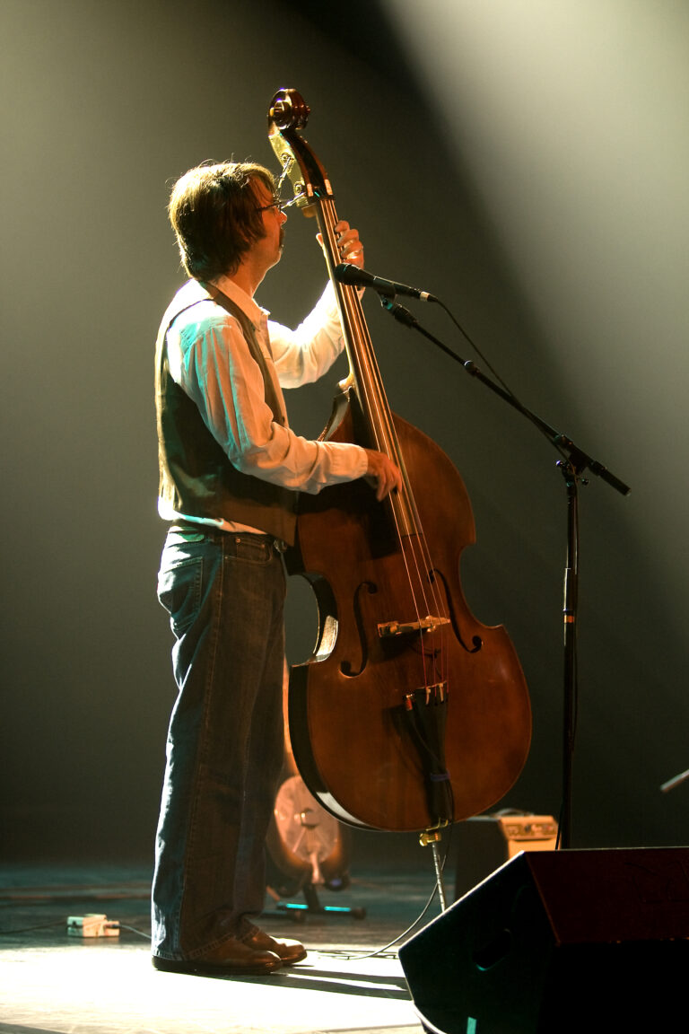 Een muzikant staat op het podium en speelt een contrabas onder spotlights.