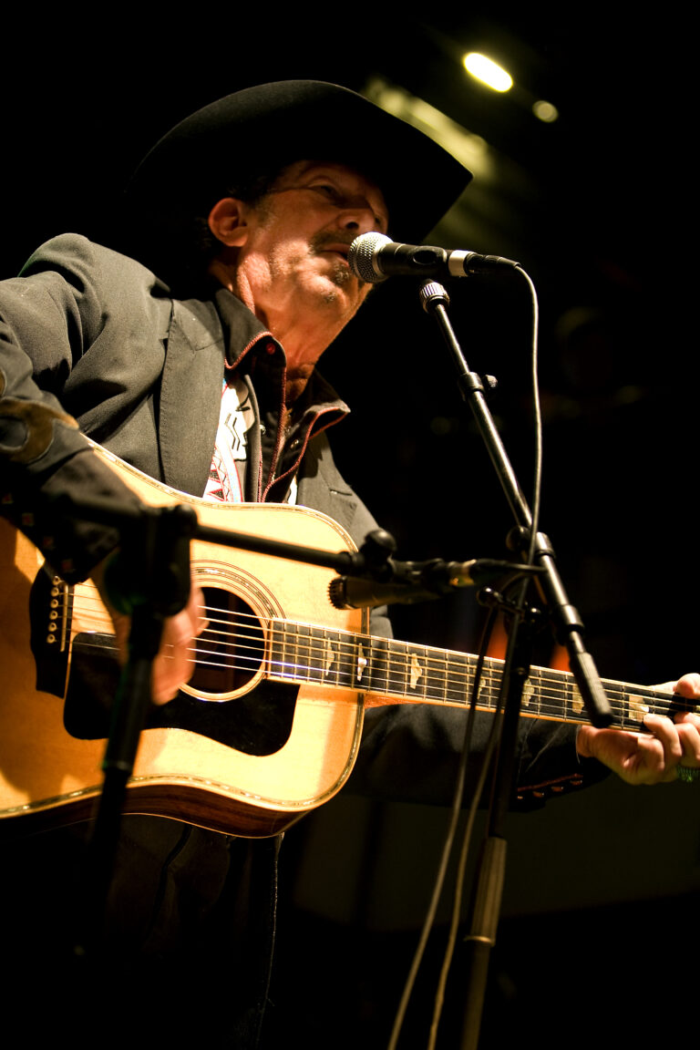 Een muzikant speelt gitaar en zingt in een microfoon op het podium.