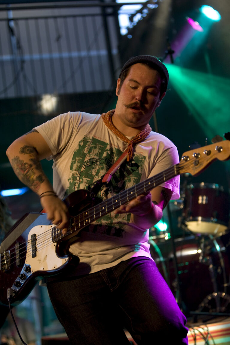 Een muzikant speelt intensief basgitaar op een podium met kleurrijke verlichting.