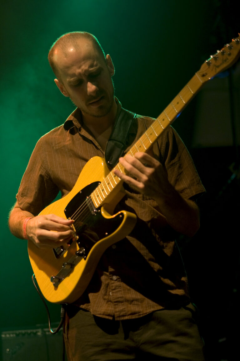 Een muzikant speelt gitaar op een podium met groene verlichting.