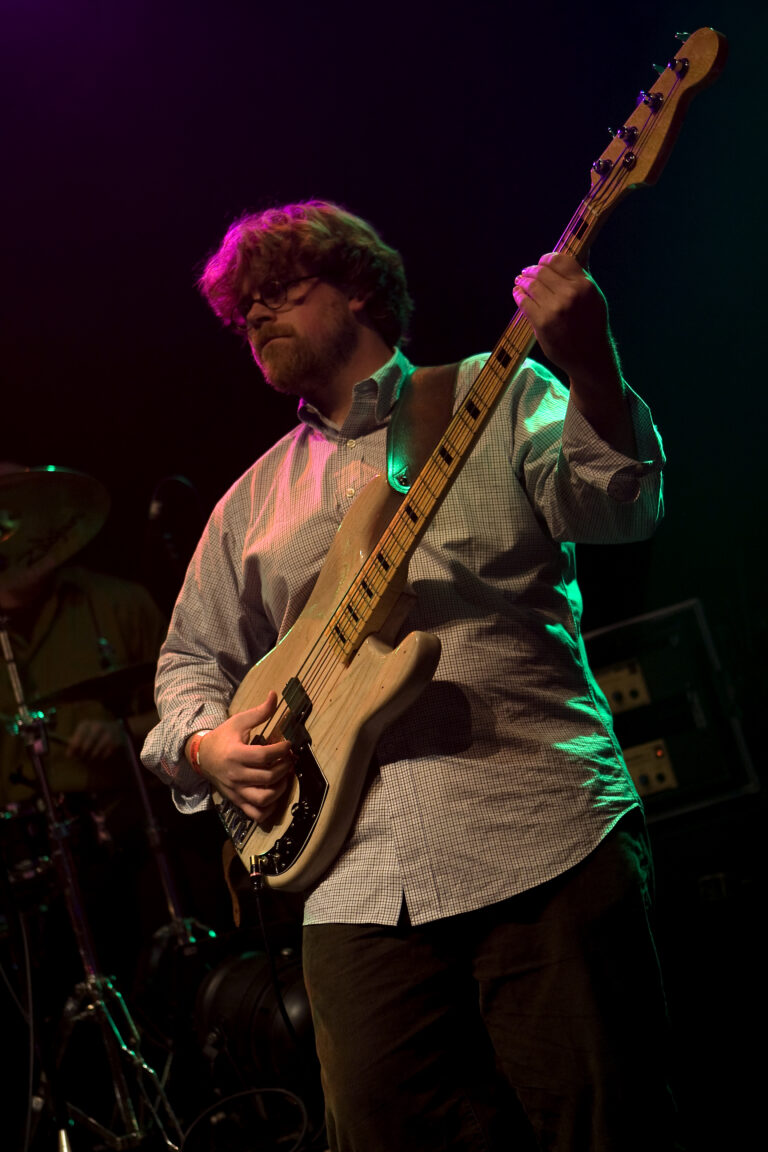 Een muzikant speelt gitaar op het podium met kleurrijke verlichting.