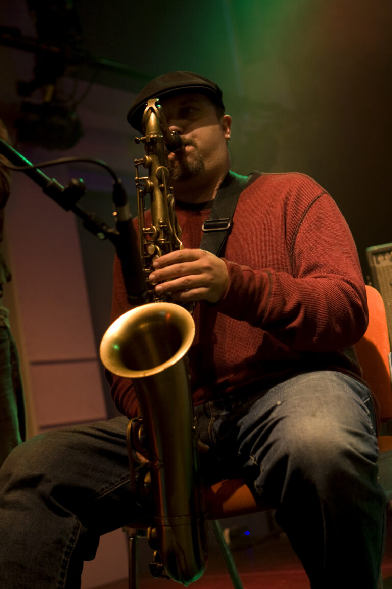 Een muzikant speelt saxophone terwijl hij op een stoel zit in een sfeervolle omgeving.