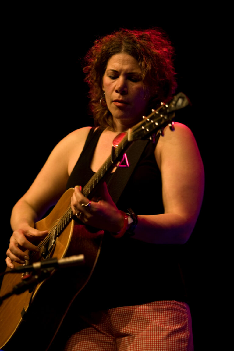 Een muzikante speelt geconcentreerd op een akoestische gitaar op het podium.