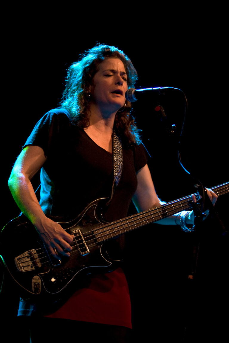 Een muzikant speelt basgitaar op het podium met neonverlichting op de achtergrond.