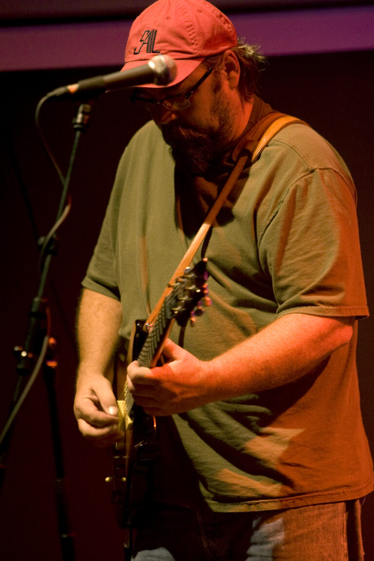 Een muzikant speelt gitaar op een podium met een warme, sfeervolle verlichting.