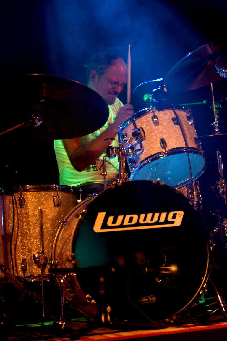 Een drummer speelt energiek op een Ludwig drumstel onder kleurrijke lichtjes.