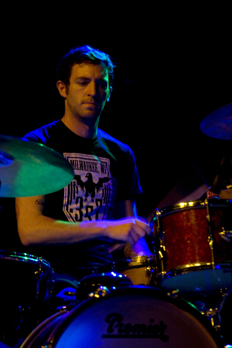 Een drummer speelt op een set van drums in een sfeervolle, verlichte omgeving.