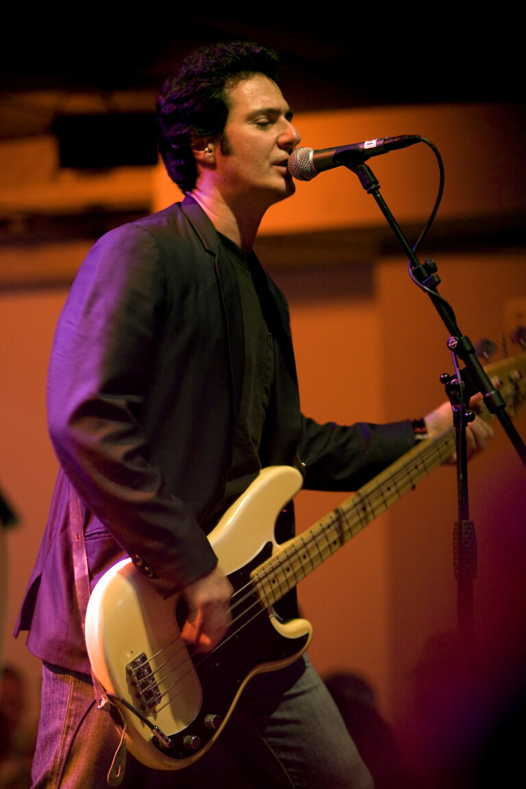 Een muzikant speelt op een elektrisch basgitaar terwijl hij zingt in een sfeervolle setting.