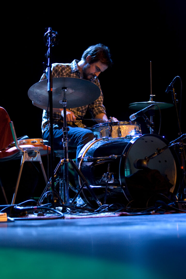 Een drummer speelt op een drumstel tijdens een optreden in een donkere zaal.