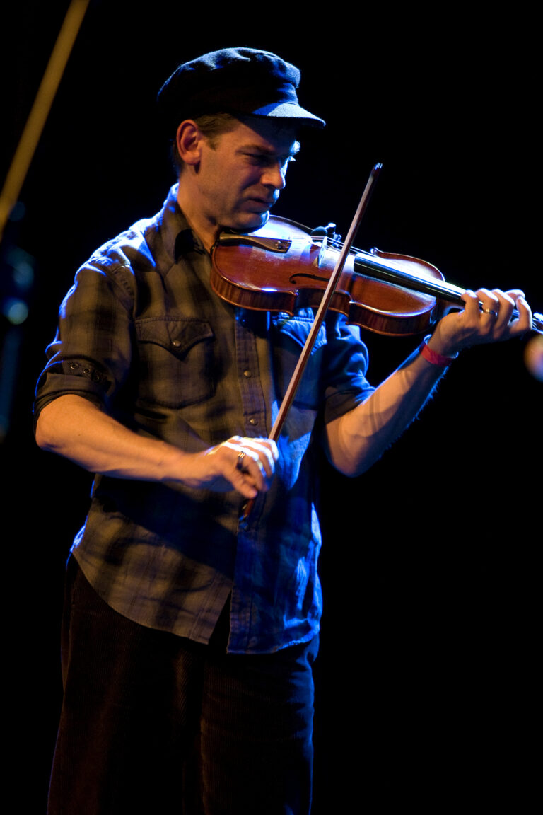 Een muzikant speelt viool op het podium in een sfeervolle, donkere omgeving.