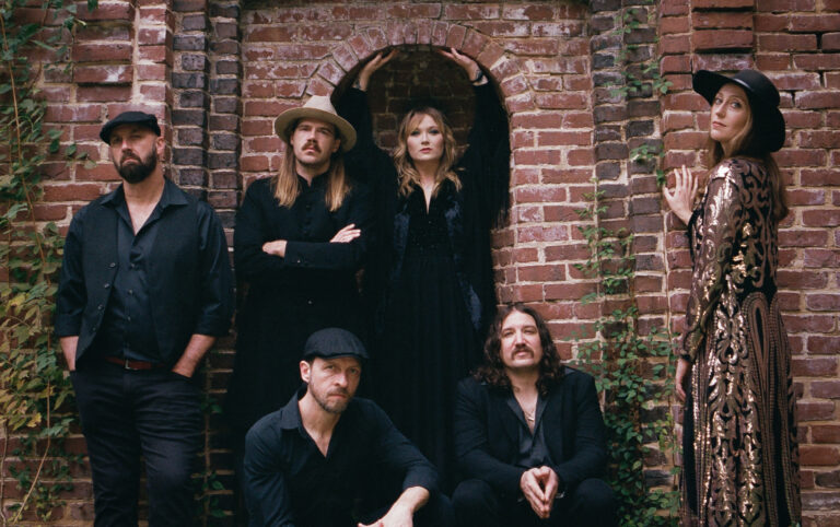 Band rumours staat voor een oud stenen muurtje, er zijn 6 bandleden en ze kijken recht in de camera.