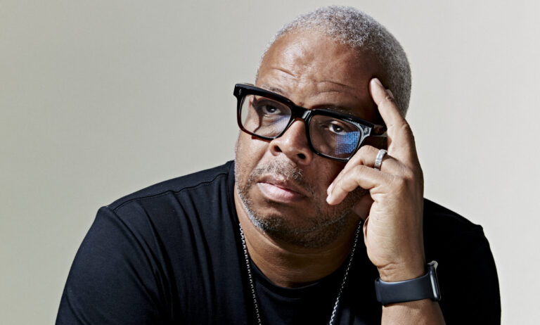 Portretfoto van trompetist. Zijn trompet ligt voor hem en hij kijkt serieus naar de camera.