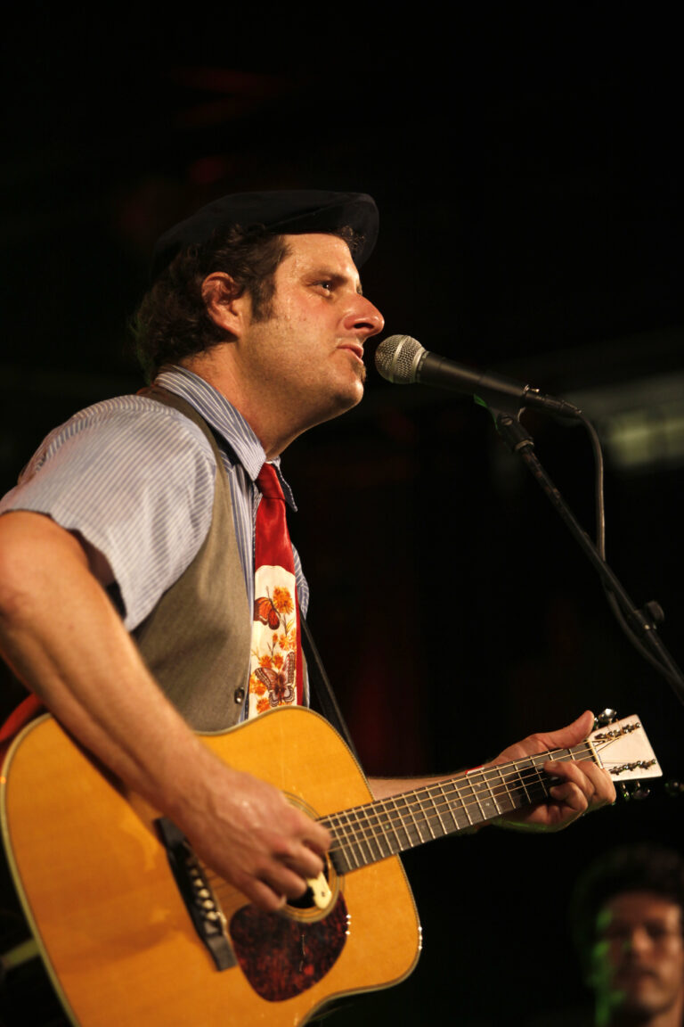 Man met gitaar die een nummer uitvoert op het podium.