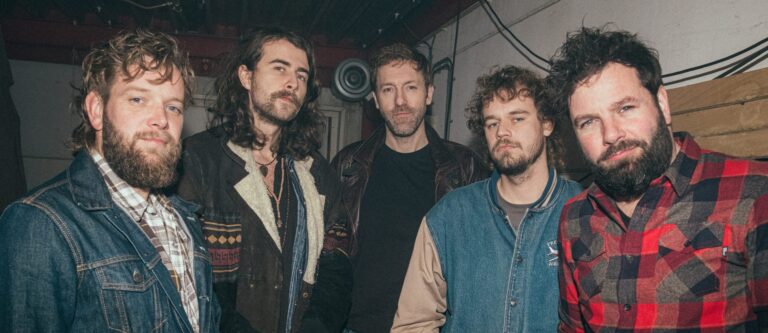 Bandfoto met vijf stoere mannen die in de camera kijken ergens in een schuur
