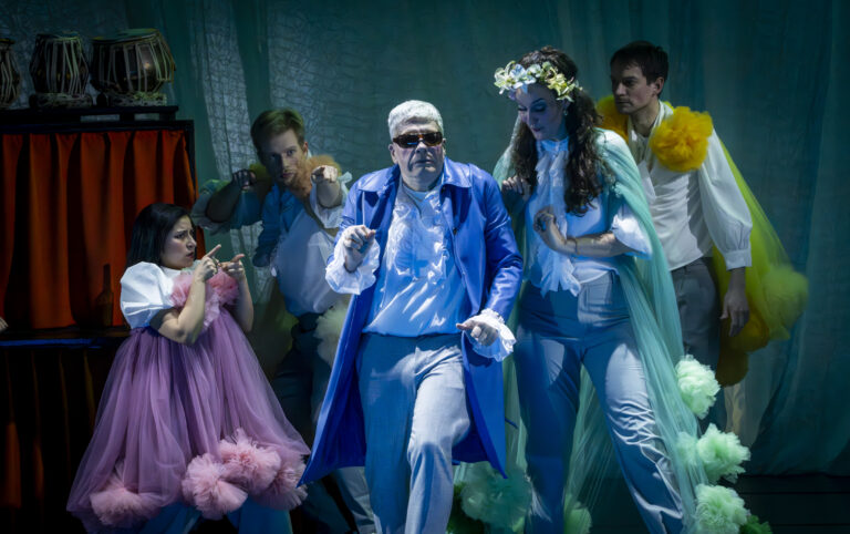 vijf mensen met gekleurde kleding staan in gekke posities