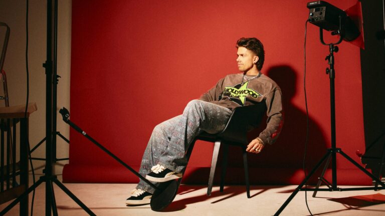 André Hazes zit onderuitgezak op een stoel in een fotostudiosetting met rode achterwand