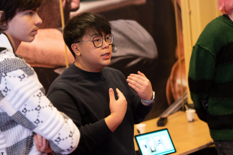 Jongen met zwarte trui en bril legt iets uit