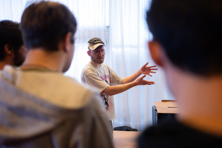 Man met pet en grijs T-Shirt steekt zijn handen naar rechts.