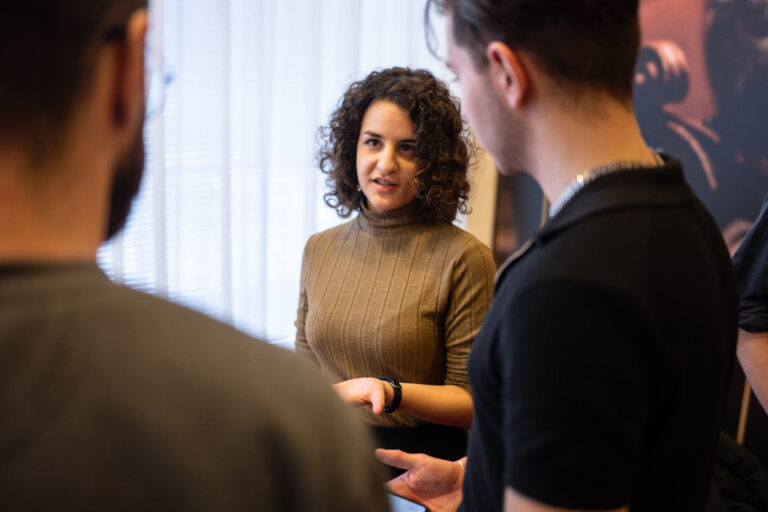 Vrouw met donker haar en krullen praat met twee mannen