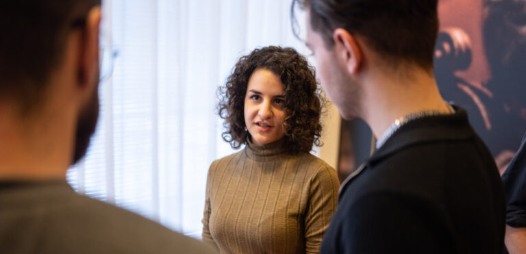 Vrouw met donker haar en krullen praat met twee mannen