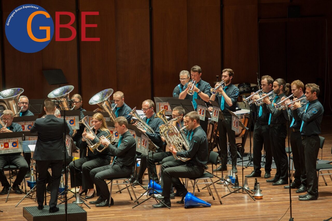 Een blaasorkest voert muziek uit op een podium, gekleed in zwarte en turquoise outfits.