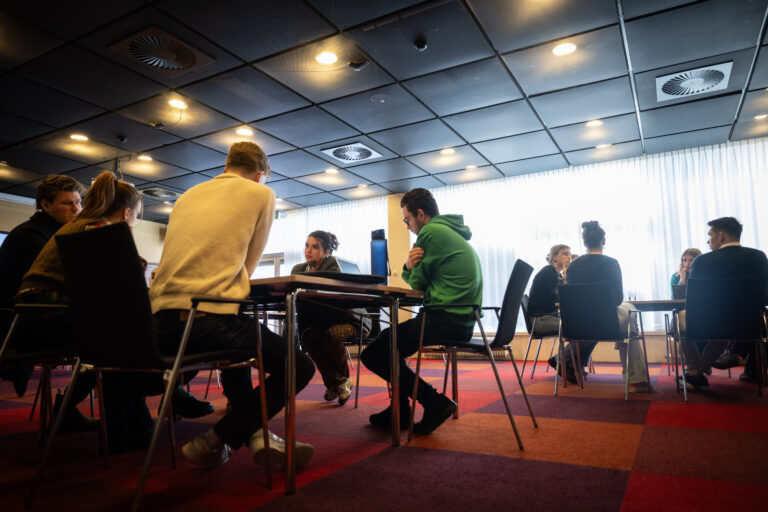 Studenten in felgekleurde truien aan een tafel