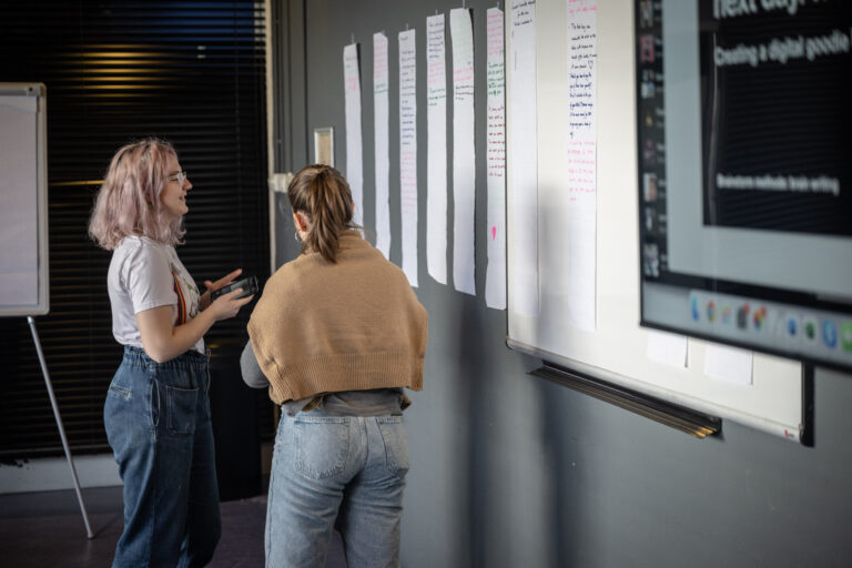 Twee personen voor een papier waar zij post-its ophangen