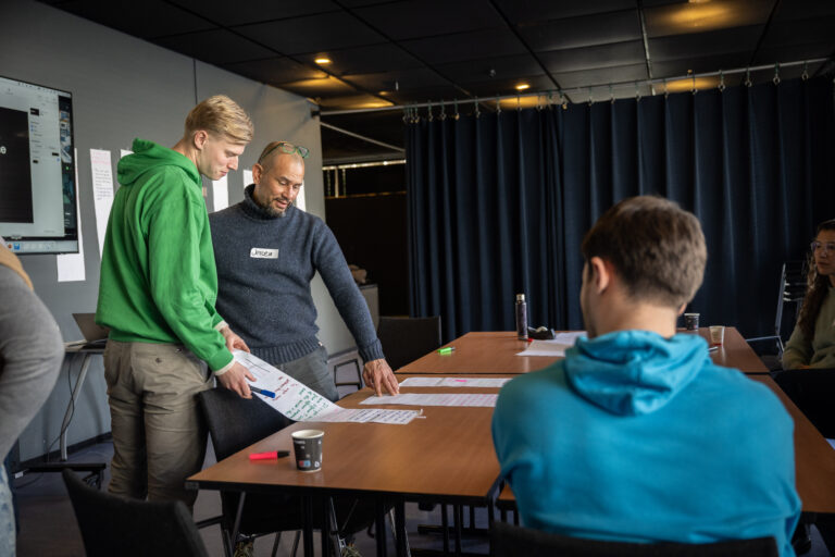 Drie studenten in felgekleurde truien aan een tafel in overleg
