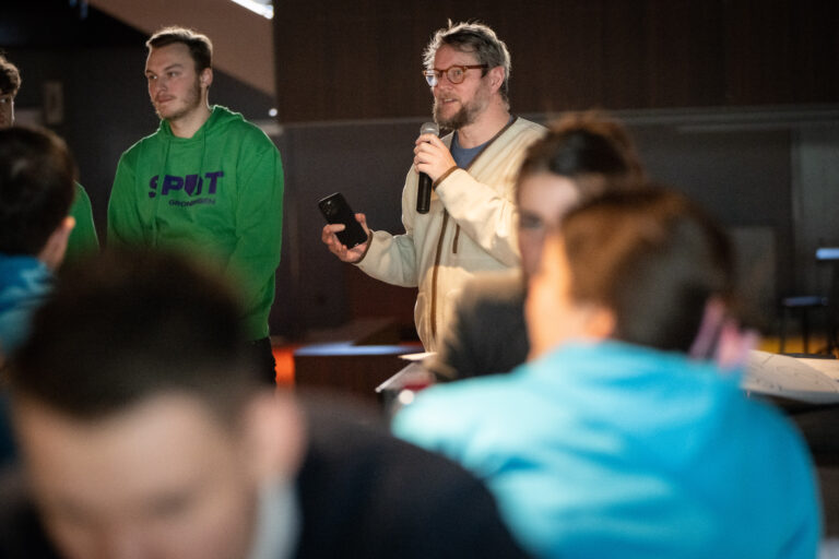Twee personen waarvan de linker een groene trui aan heeft en de rechter een microfoon
