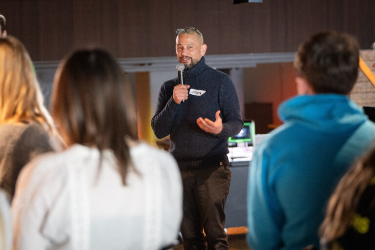 Persoon in donkerblauwe trui staat met microfoon in zijn hand te presenteren