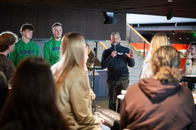 Persoon in donkerblauwe trui staat met microfoon te presenteren