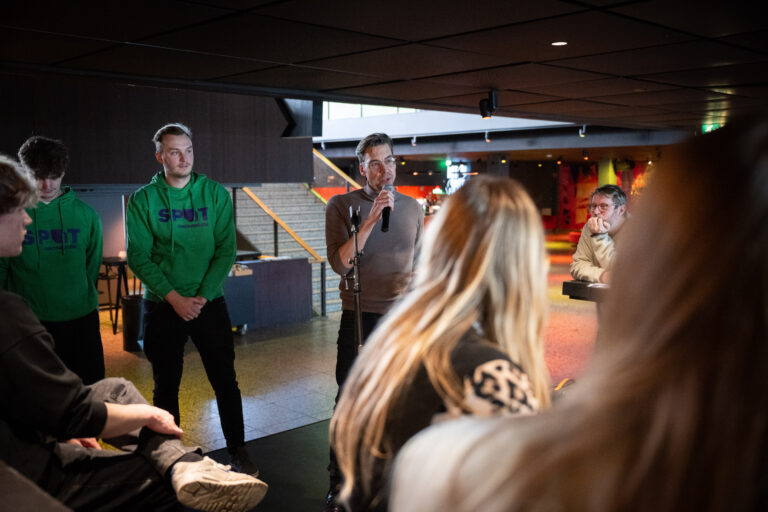 Twee personen in groene trui en grijze trui staan te presenteren