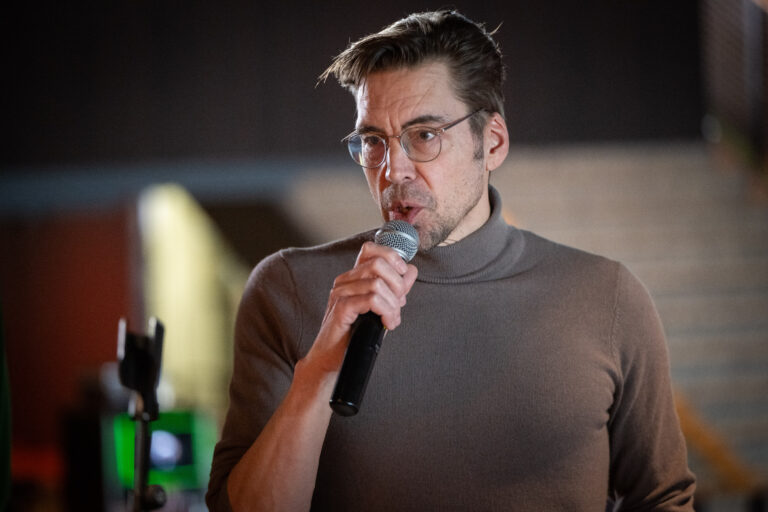 Persoon in grijze trui vertelt met microfoon